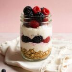 A glass jar with yogurt, berries, and granola, a nutritious breakfast or snack from a nutritional coaching plan.